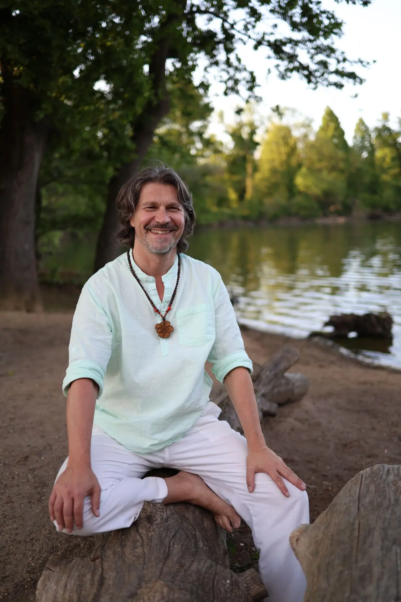 spiritueller-mentor-ralph-riedel Ralph Riedel, Schamane und spiritueller Lehrer, sitzt fröhlich am See.